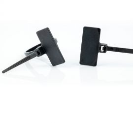 Twee zwarte kunststof kabelbinders met markeerlabel, met het label boven de kop van de kabelbinder, waarvan één los, en één gebonden.